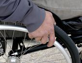 Nahaufnahme von Hand einer Person im Rollstuhl sitzend. Die Hand liegt auf dem Rollstuhlrad auf.