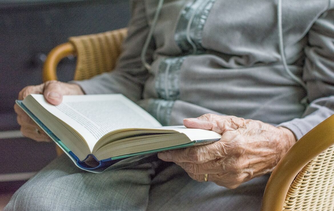 Nachaufnahme einer Seniorin, in einem Rattanstuhl sitzend, die ein Buch liest.