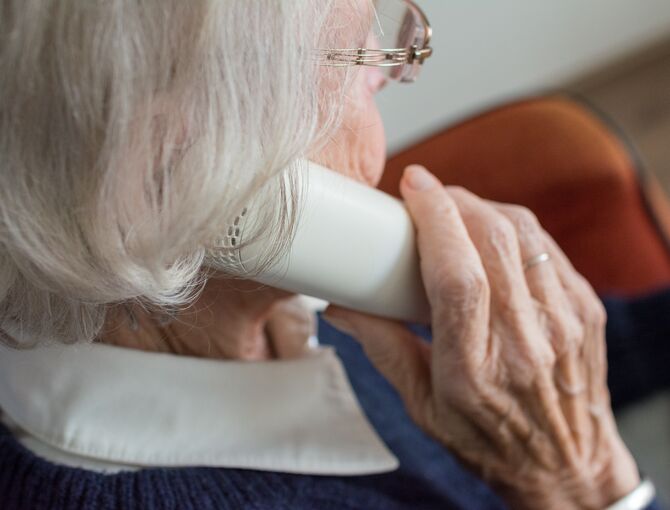 Nachaufnahme einer Senioren von schräg hinten, die ein Festnetz-Telefon an ihr Ohr hält.