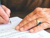 Nahaufnahme einer älteren Person, die einen Vertrag mit einem Kugelschreiber unterschreibt.